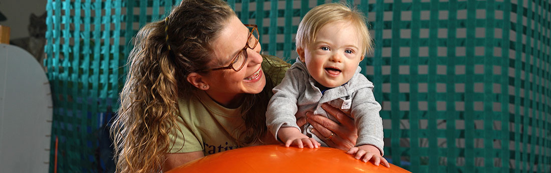 Infant with Down syndrome on large exercise ball with therapist