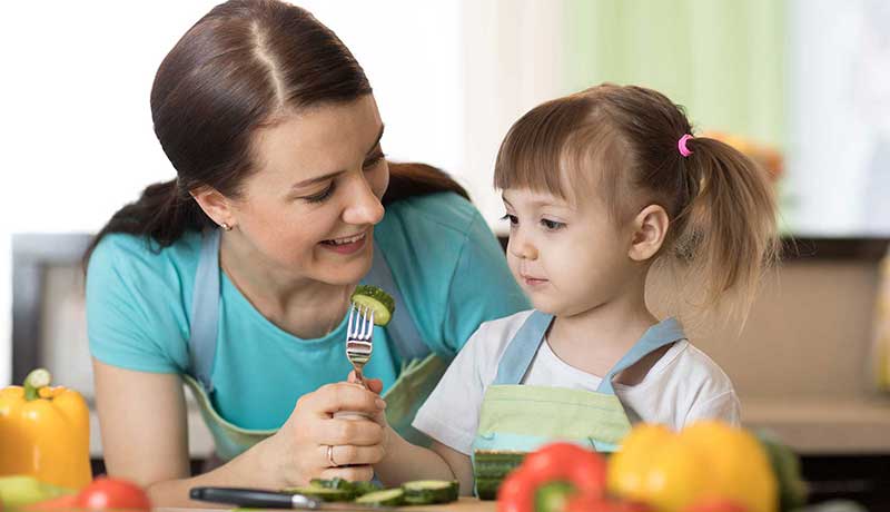 Mother holding fork with vegetable for young girl