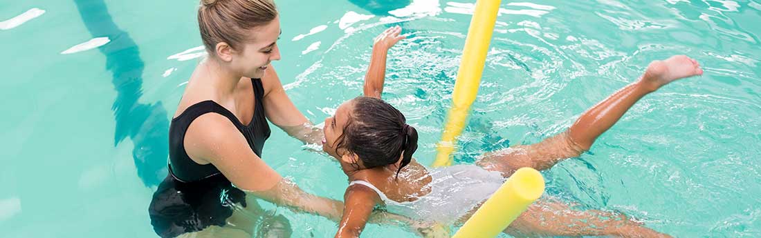 Young girl using floating device working with therapist in the pool
