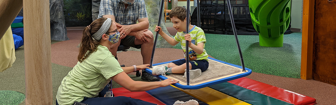 Young boy on platform swing with occupational therapist pushing