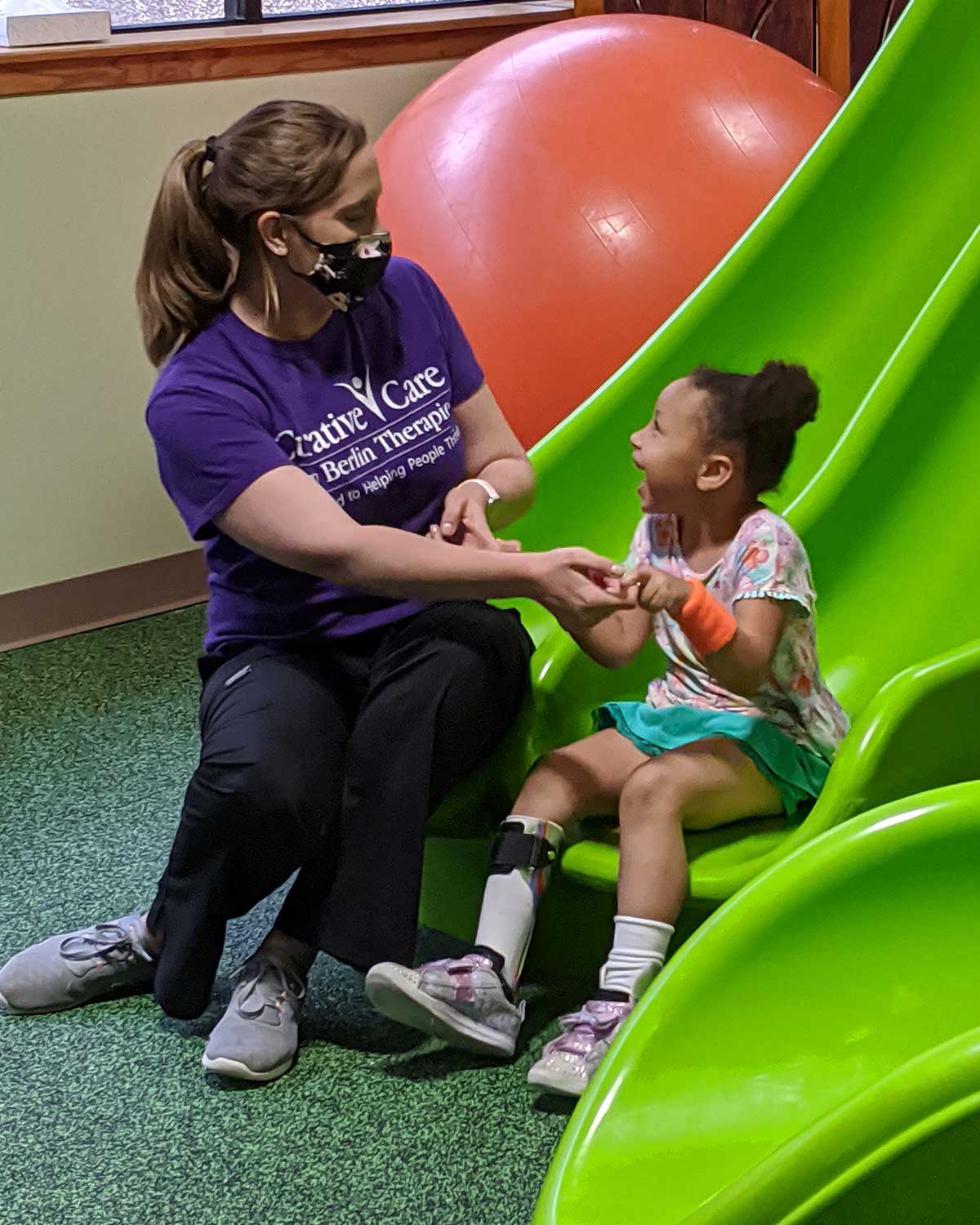Female therapist with young girl at bottom of jungle gym slide
