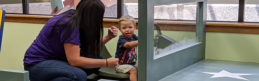 Female speech therapist with young boy driving in large wooden truck structure