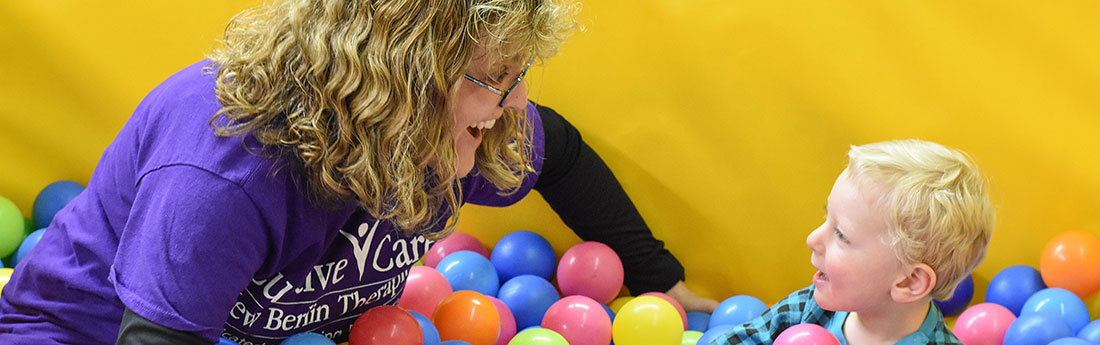 Young boy playing in ball pit with female therapist