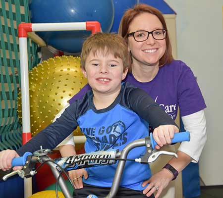 Jason on bicycle with therapist assisting