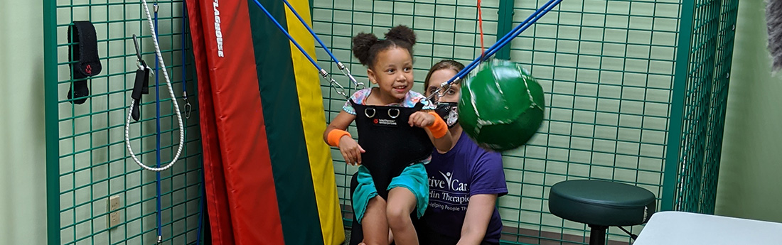 Young girl in a Universal Exercise Unit (UEU) with physical therapist