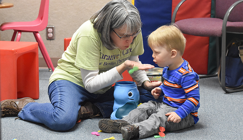 Young boy blowing object out of female therapist's hand