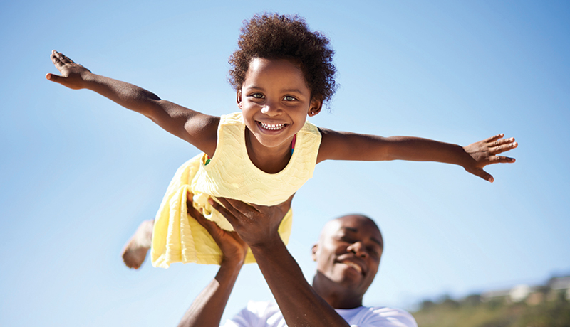 Young girl with arms out being held up by father